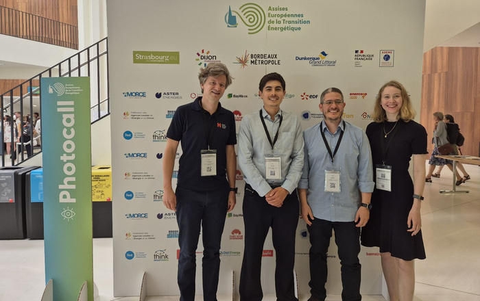 2025-07-08 PM Hochschule mit Thema Wasserstoff bei Europäischer Energiewendekonferenz und auf dem Markt Team Drei Männer und eine Frau stehen vor einer Stellwand mit den Logos der Beteiligten der Energiewendekonferenz